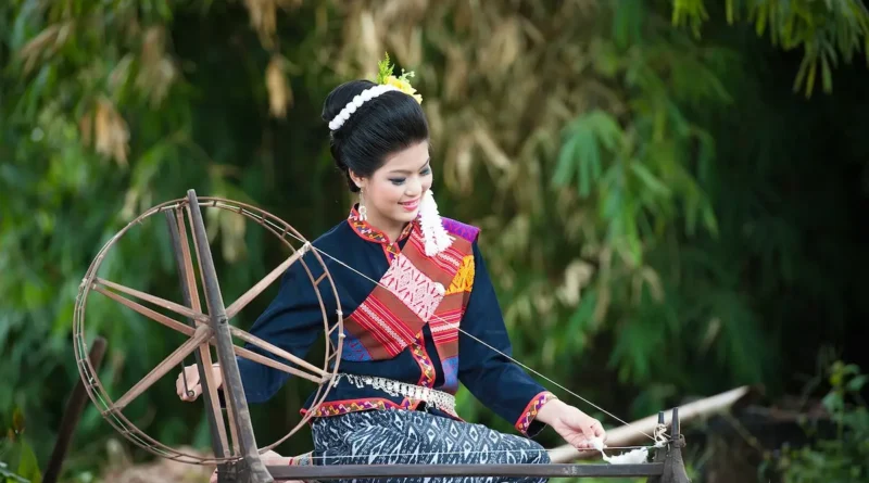 Seorang wanita yang sedang menenun benang menggunakan alat seperti roda